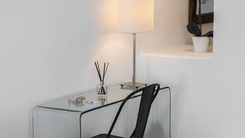 A modern, minimalist room with a glass desk, a black chair, a lamp, and a small potted plant.