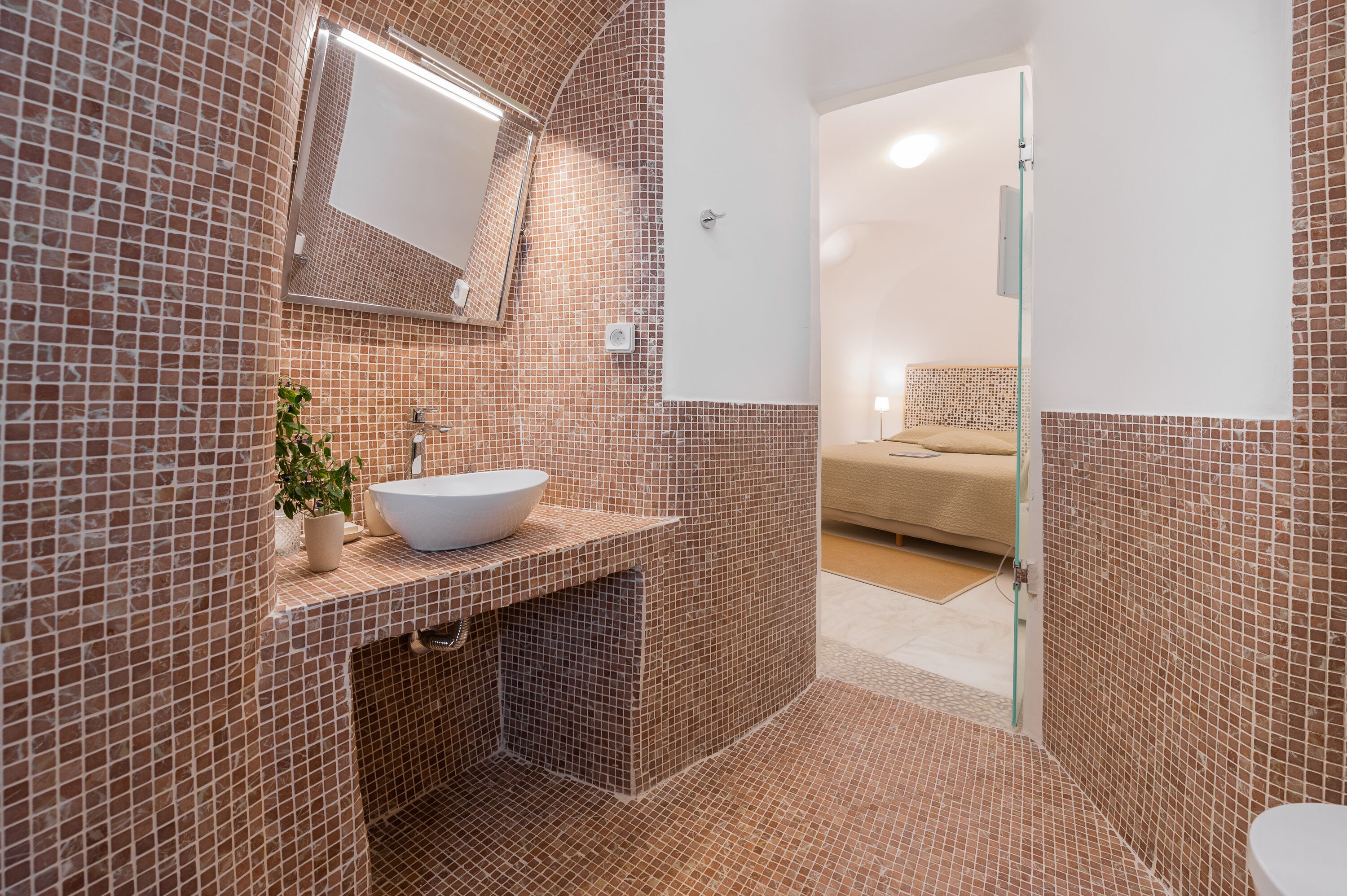 Un baño con pared de azulejos, un lavamanos, un espejo y una zona de ducha.