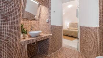 Un baño con pared de azulejos, un lavamanos, un espejo y una zona de ducha.