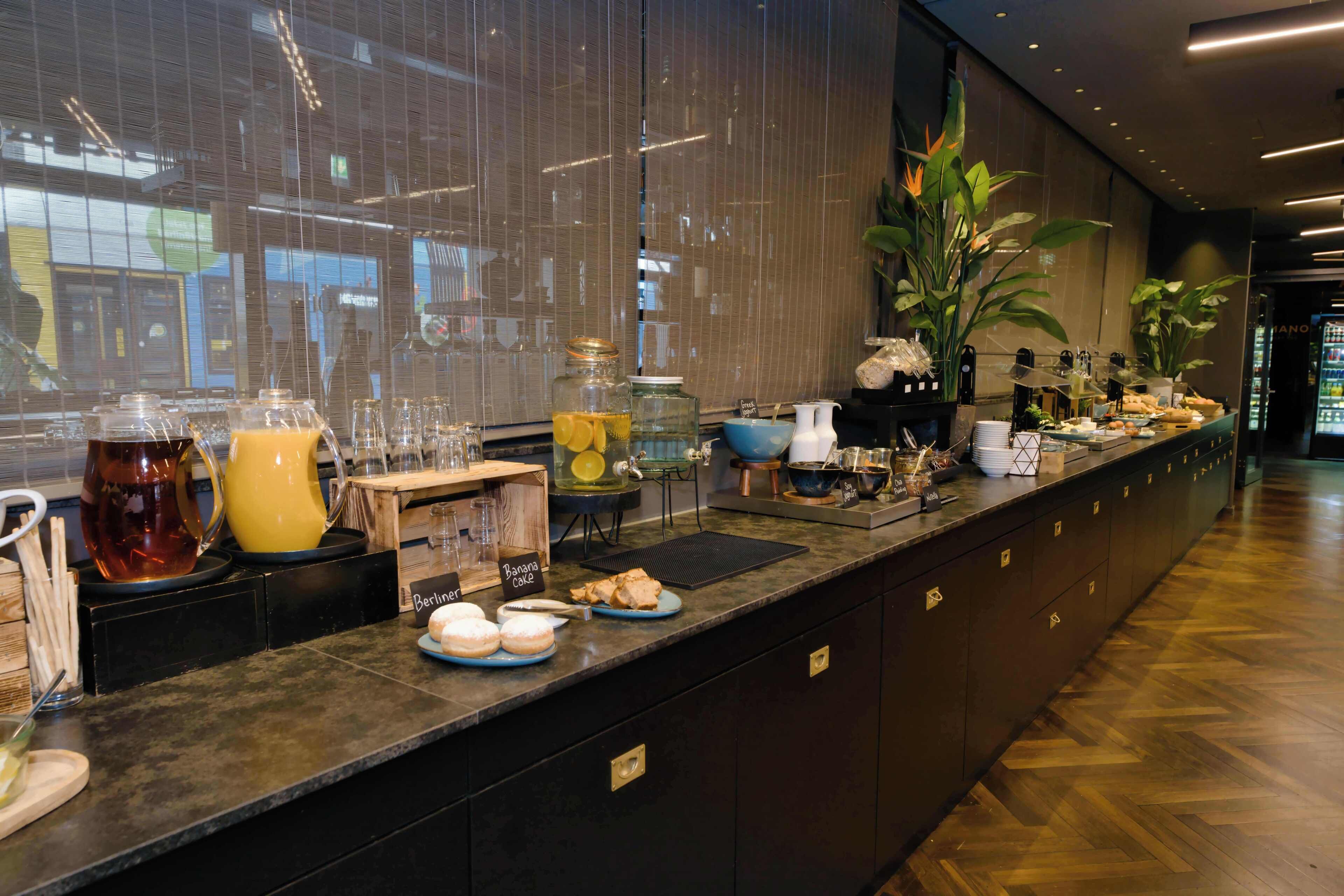 A buffet counter with various food items, a coffee station, and a refrigerator in the background.