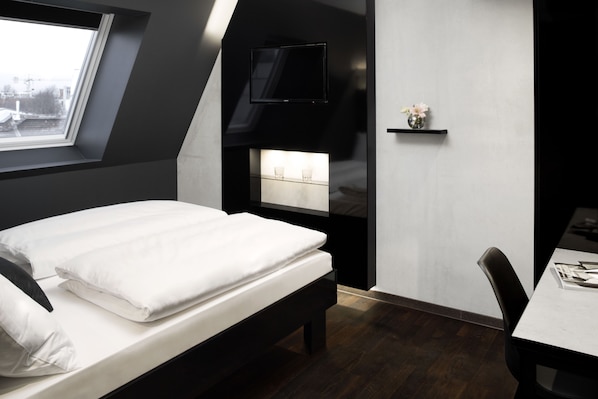 Un dormitorio moderno con una cama, un televisor montado en la pared, una mesita y un ventanal con vista a la ciudad.