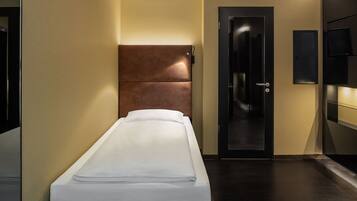 Un llit individual en una habitació d'hotel, amb capçalera, una porta i televisió penjada a la paret.