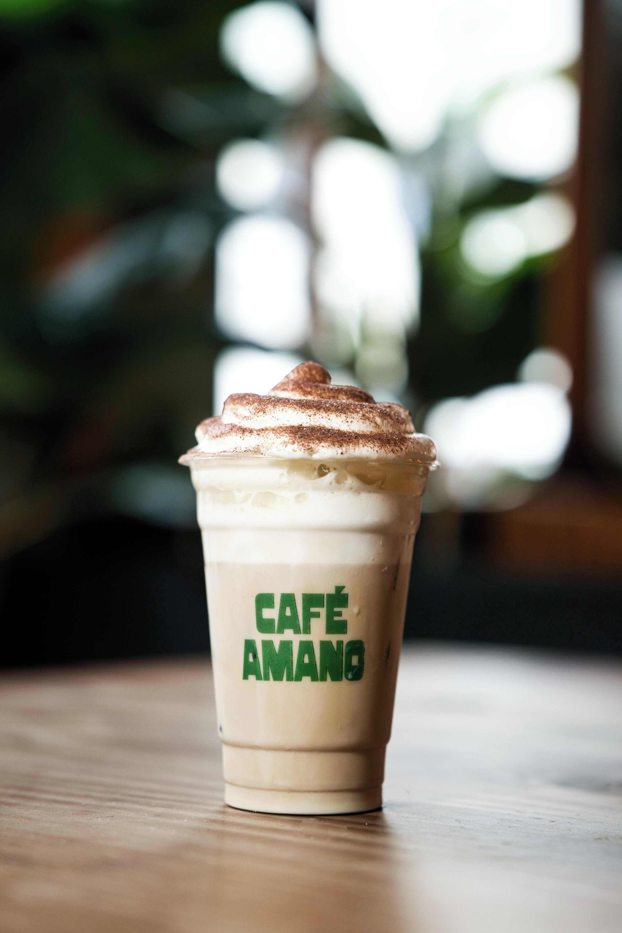 Une tasse de café glacé, surmontée de crème fouettée et d’une pincée de cannelle, avec l’étiquette « CAFÉ AMANO ».