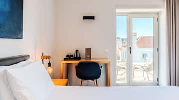 Habitación de hotel con cama, escritorio con silla, cafetera y vistas al exterior.