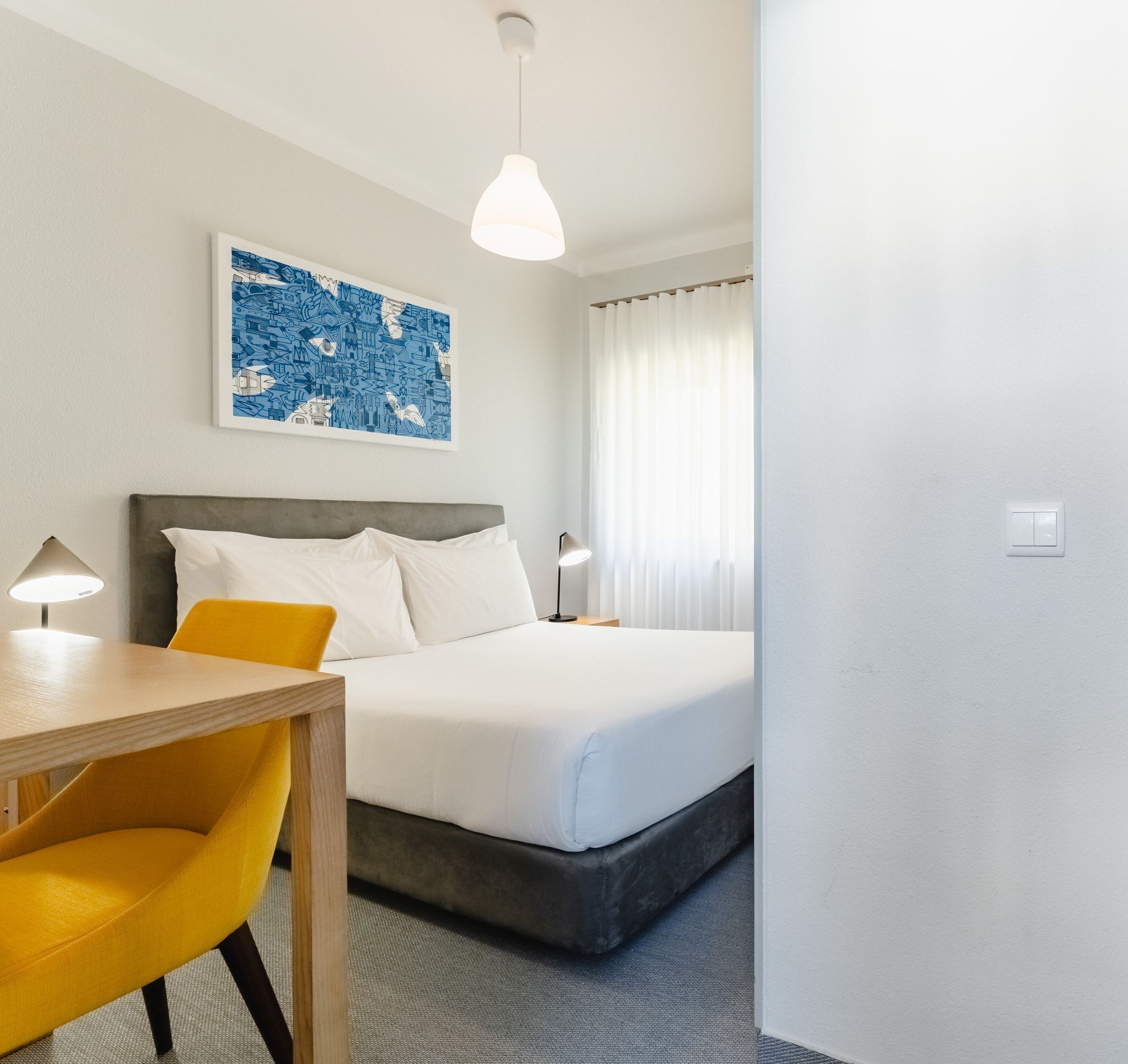 Een hotelkamer met een bed, een bureau, een stoel, een lamp en een schilderij aan de muur.