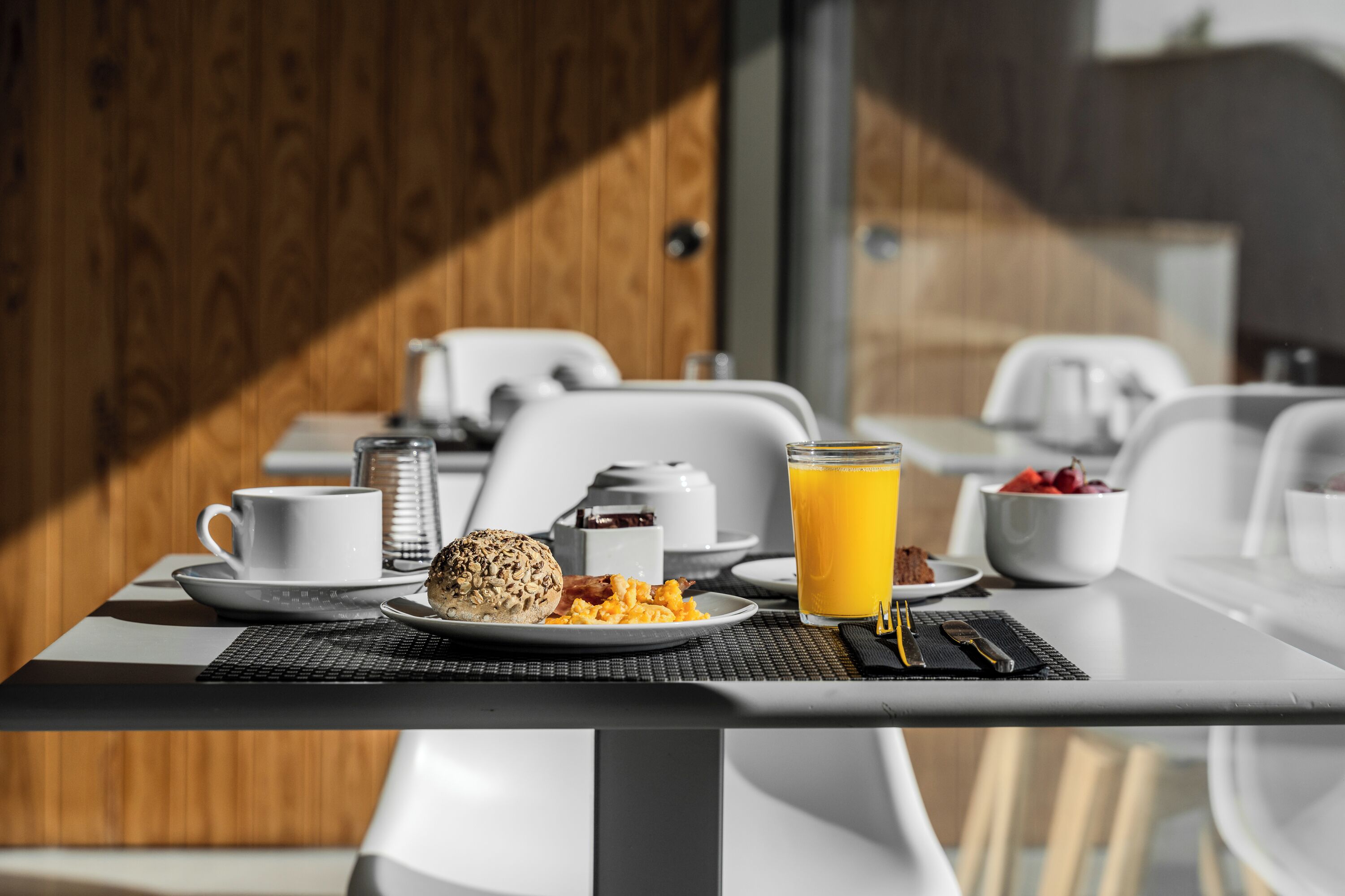 Ein Frühstückstisch mit Rührei, einem Muffin, einem Glas Orangensaft und einer Schale Erdbeeren.