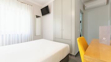 Una habitación de hotel con cama, escritorio, silla, televisor montado en la pared y armario.