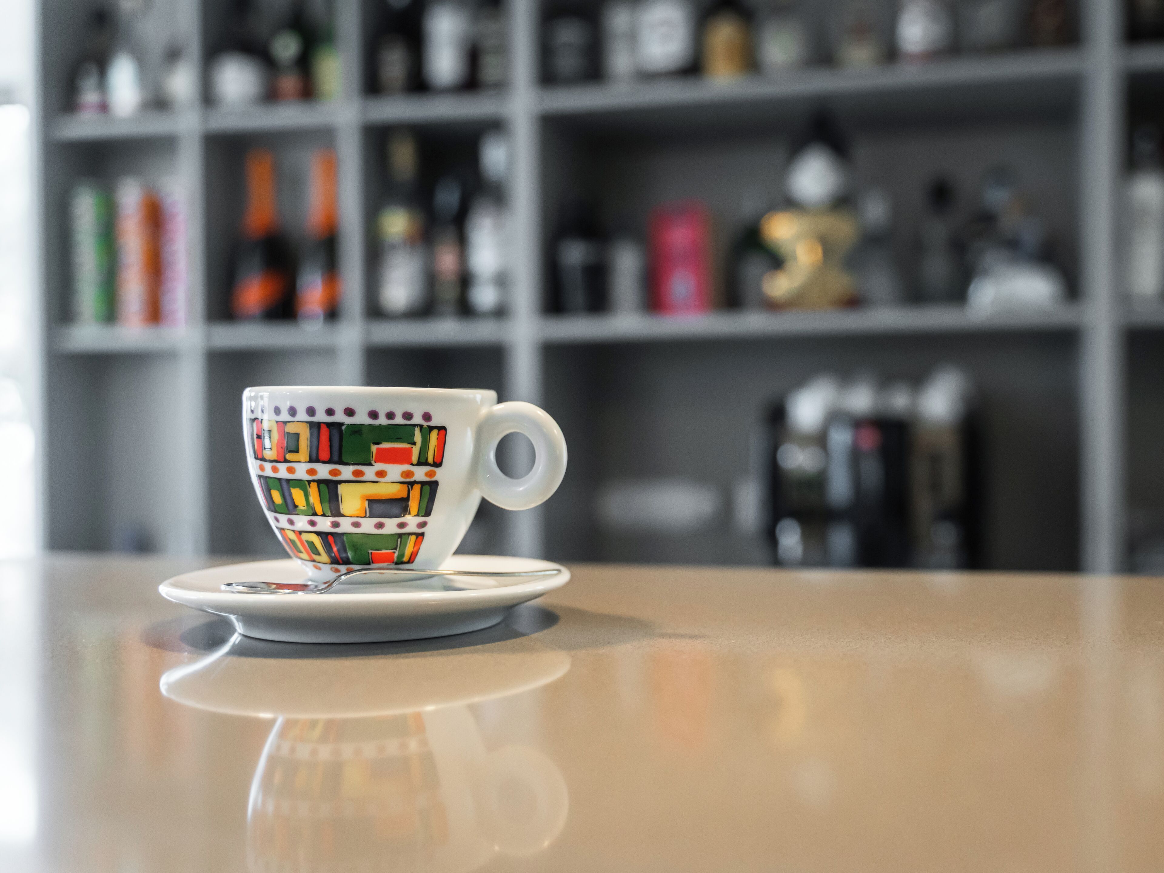 Una taza de cerámica con un estampado geométrico colorido sobre una superficie reflectante.