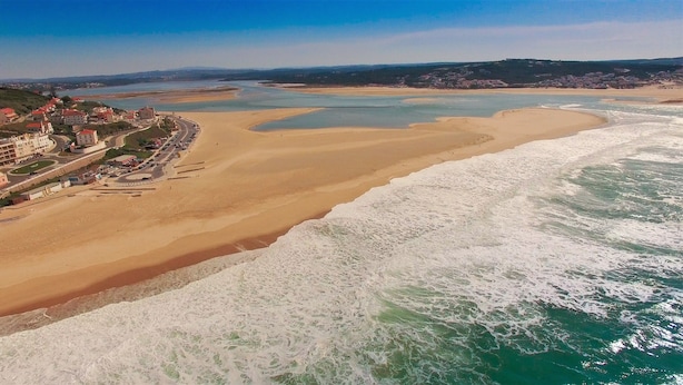 Vista aérea de una zona costera con playa arenosa, una carretera con vehículos y edificios a lo largo de la costa.