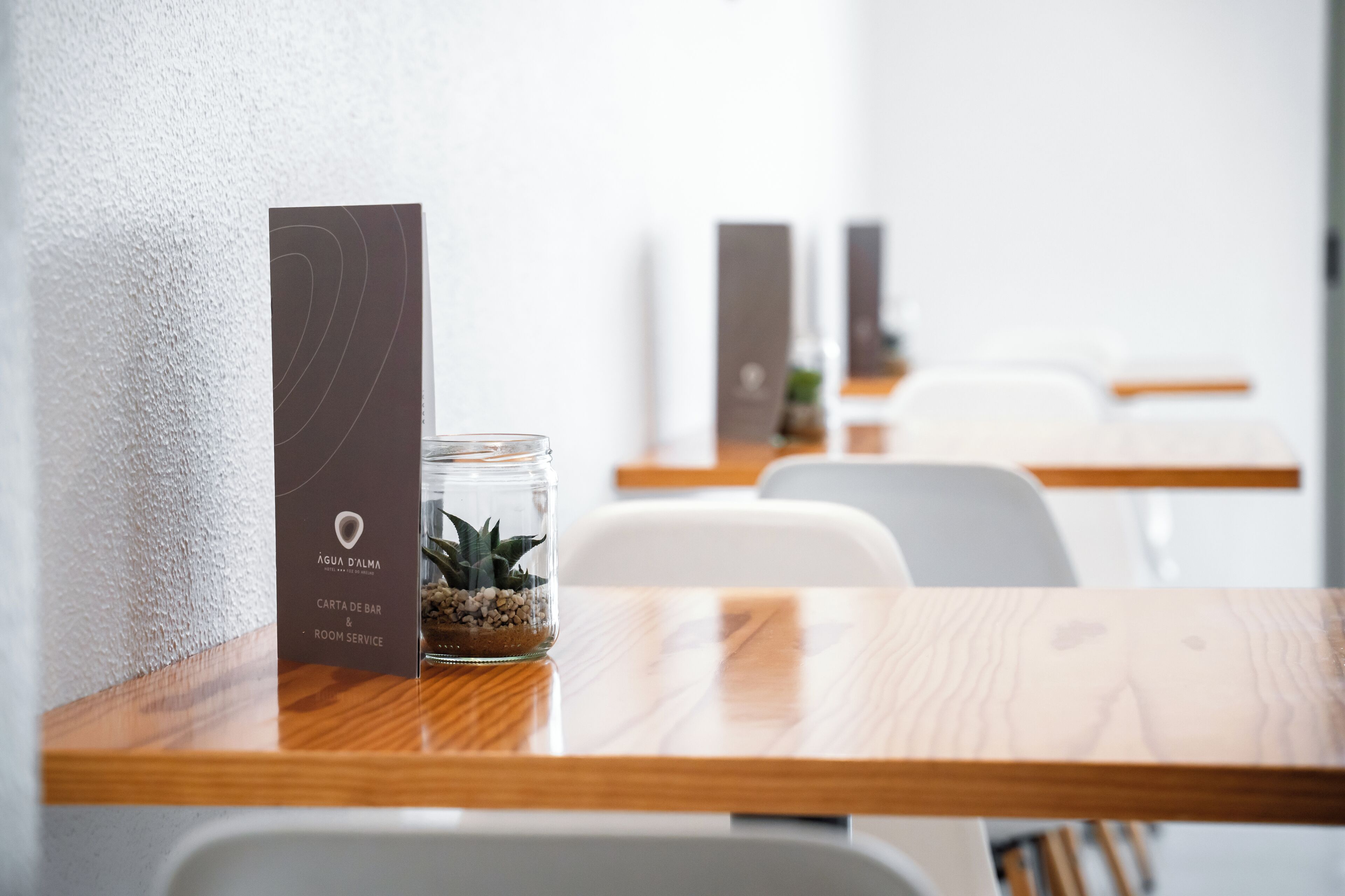 A wooden table with a glass jar containing a plant and a card for bar and room service.