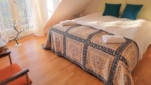 Une chambre avec un grand lit, une vue sur l’extérieur par une fenêtre et un petit arbre décoratif.