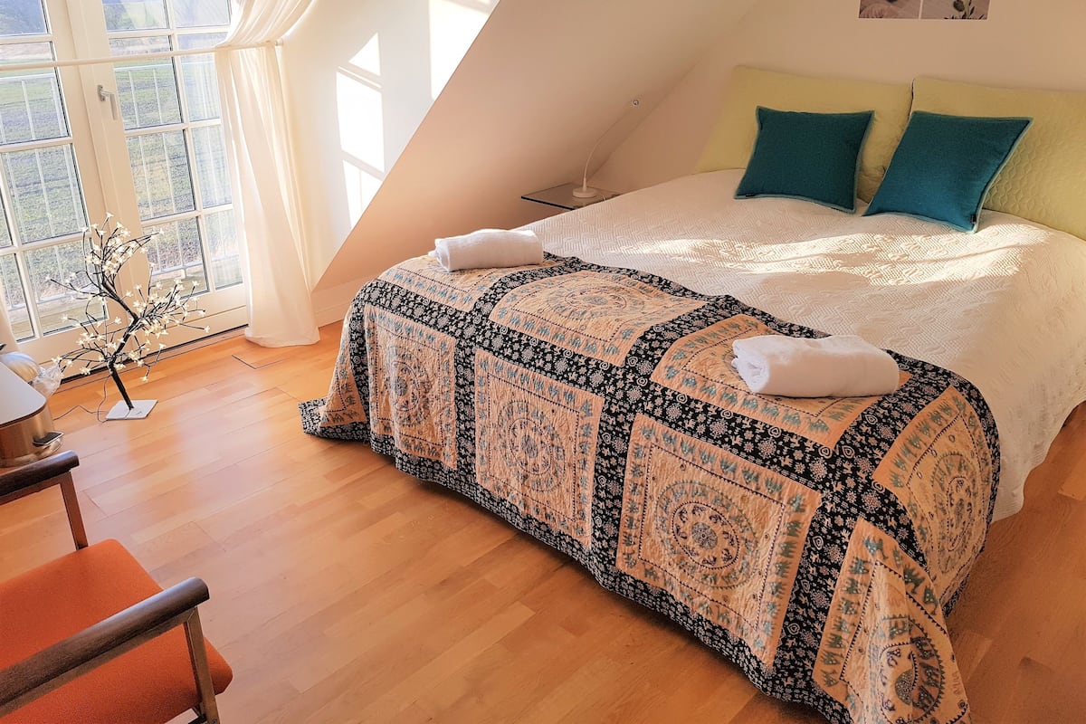 Quarto com uma cama grande, vista do exterior por uma janela e uma pequena decoração de árvore.
