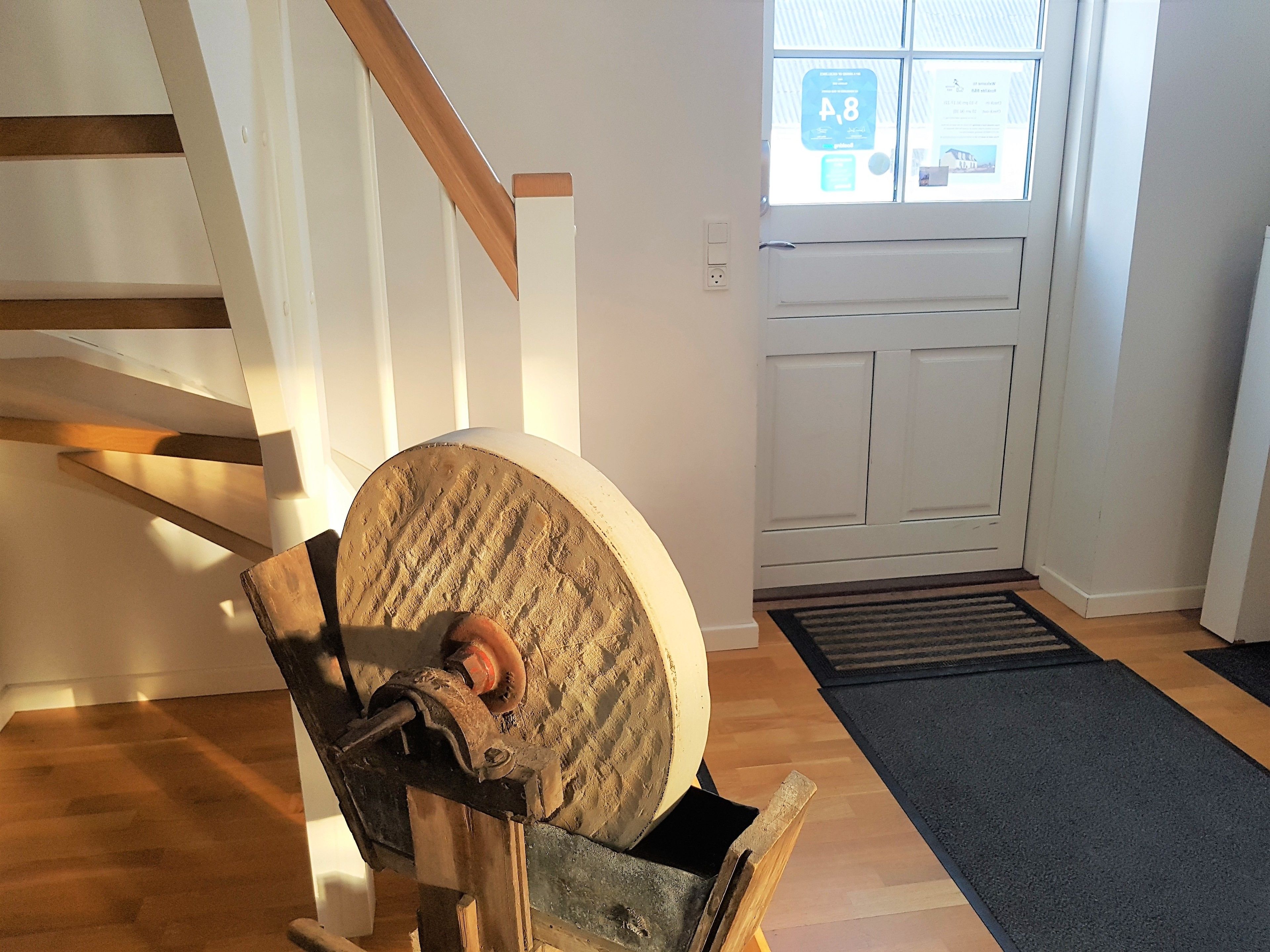 Una silla de madera con cojín, una escalera, una puerta con ventanal y un felpudo.