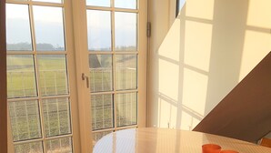 Une pièce dotée d’une grande fenêtre, d’une table ronde sur laquelle se trouve un plateau rempli de tasses oranges, et d’un plancher en bois.