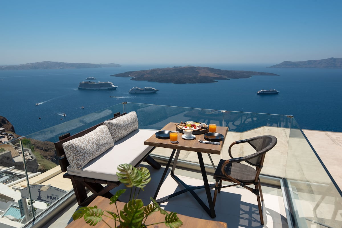 A dining area with a table set for two, overlooking a scenic view of the sea with several boats.