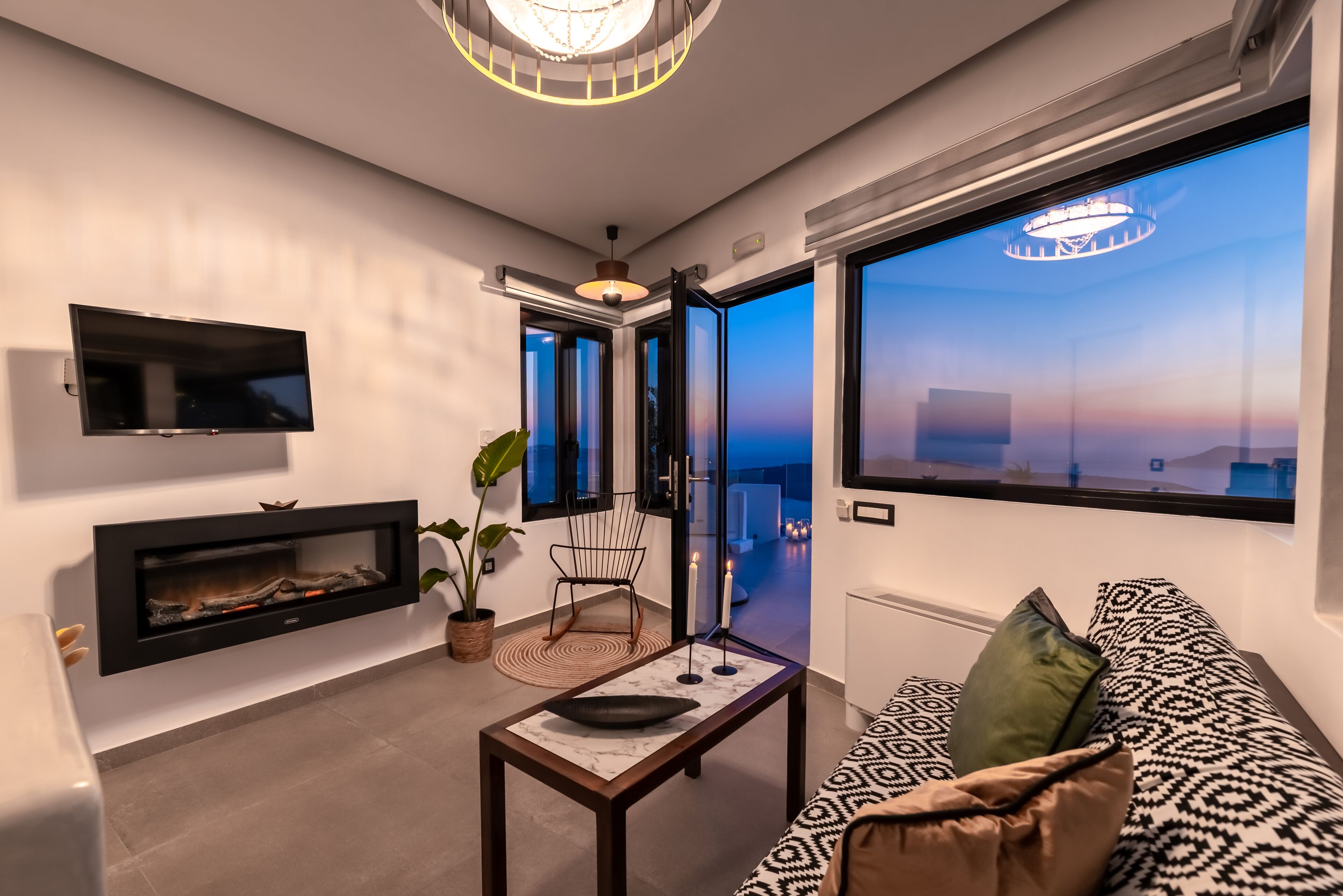 Ein modernes Wohnzimmer mit Kamin, Fernseher, einer Couch und einem großen Fenster mit Blick.