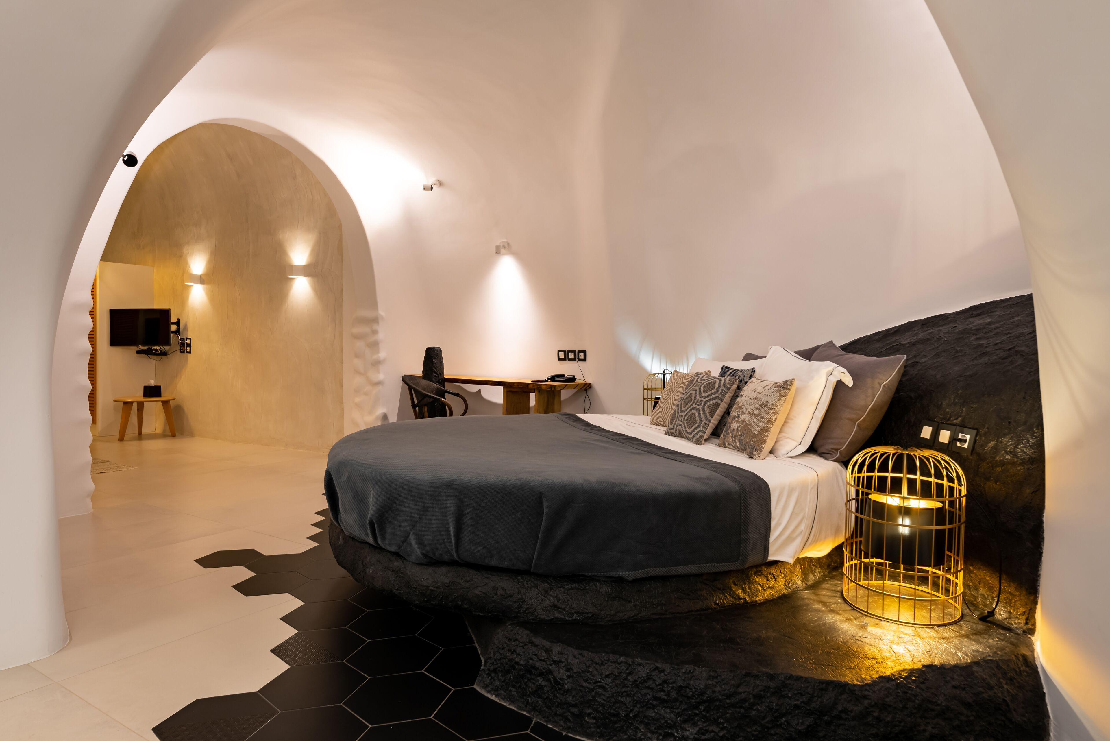 A modern bedroom with a bed, a desk, and a unique curved ceiling.