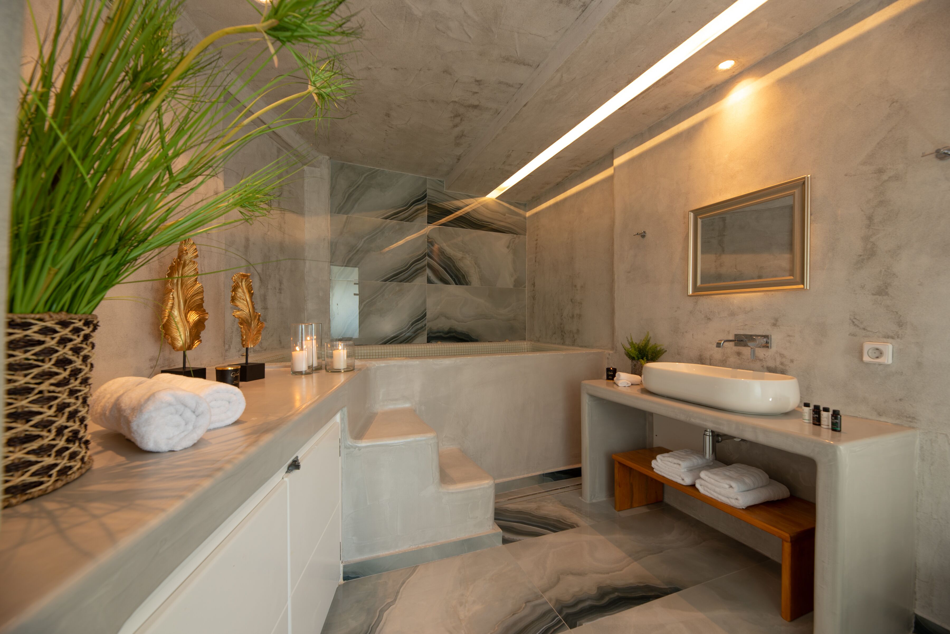 Un bagno moderno con pavimento in marmo, una vasca, un lavandino e uno specchio. Sul mobile ci sono asciugamani e una pianta.