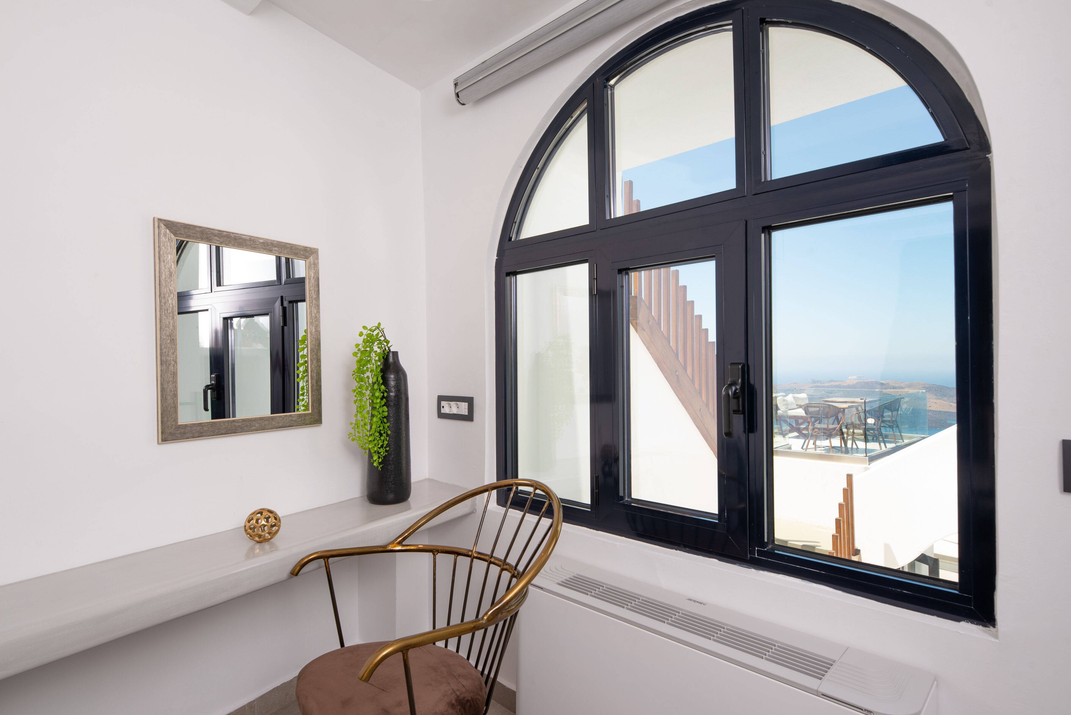 Une pièce avec une grande fenêtre en arc de cercle, un miroir, une plante et une chaise.