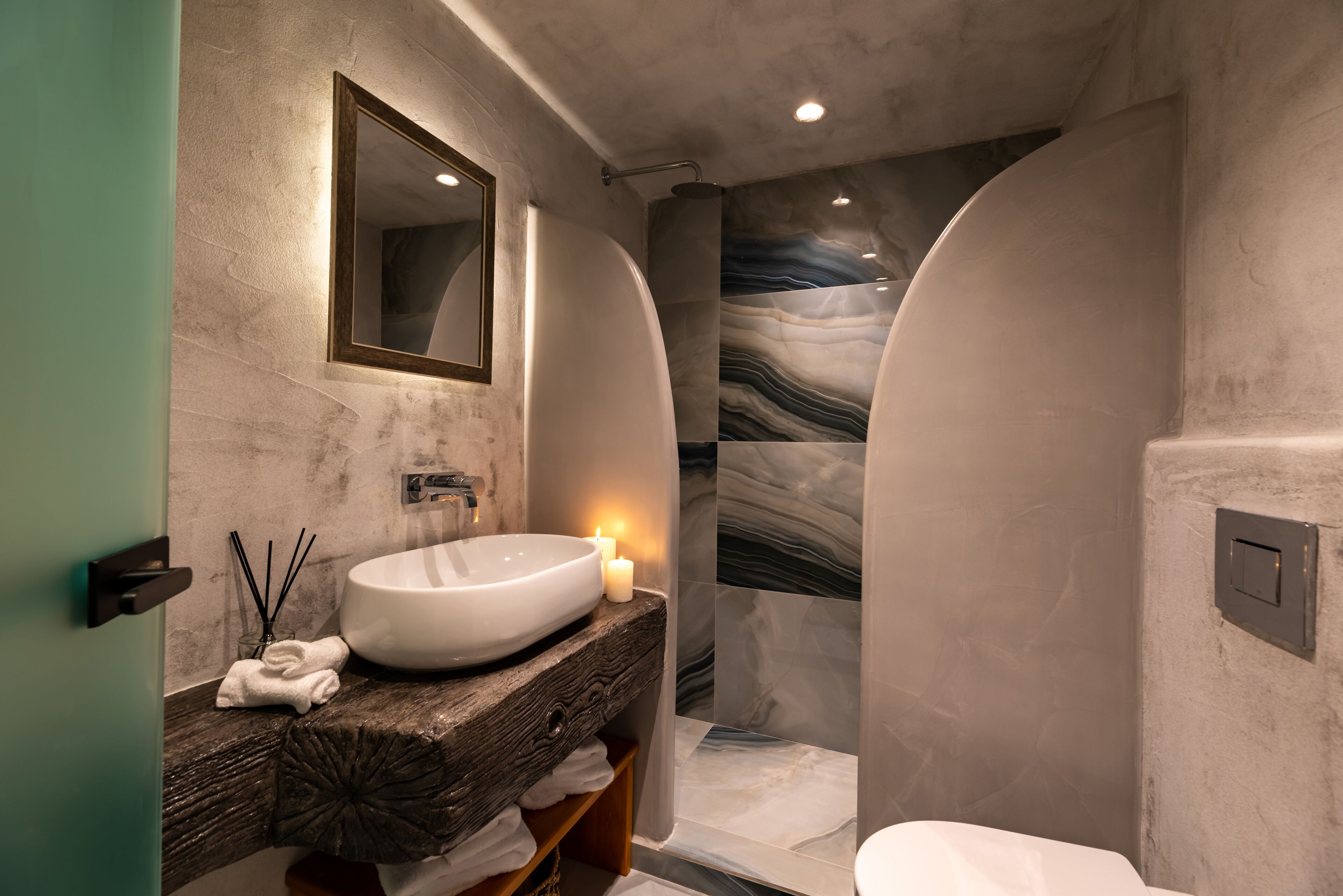 Une salle de bain moderne avec un grand lavabo ovale, un meuble-lavabo en bois, un miroir et une douche dont le mur est recouvert de marbre.