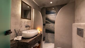 Une salle de bain moderne avec un grand lavabo ovale, un meuble-lavabo en bois, un miroir et une douche dont le mur est recouvert de marbre.