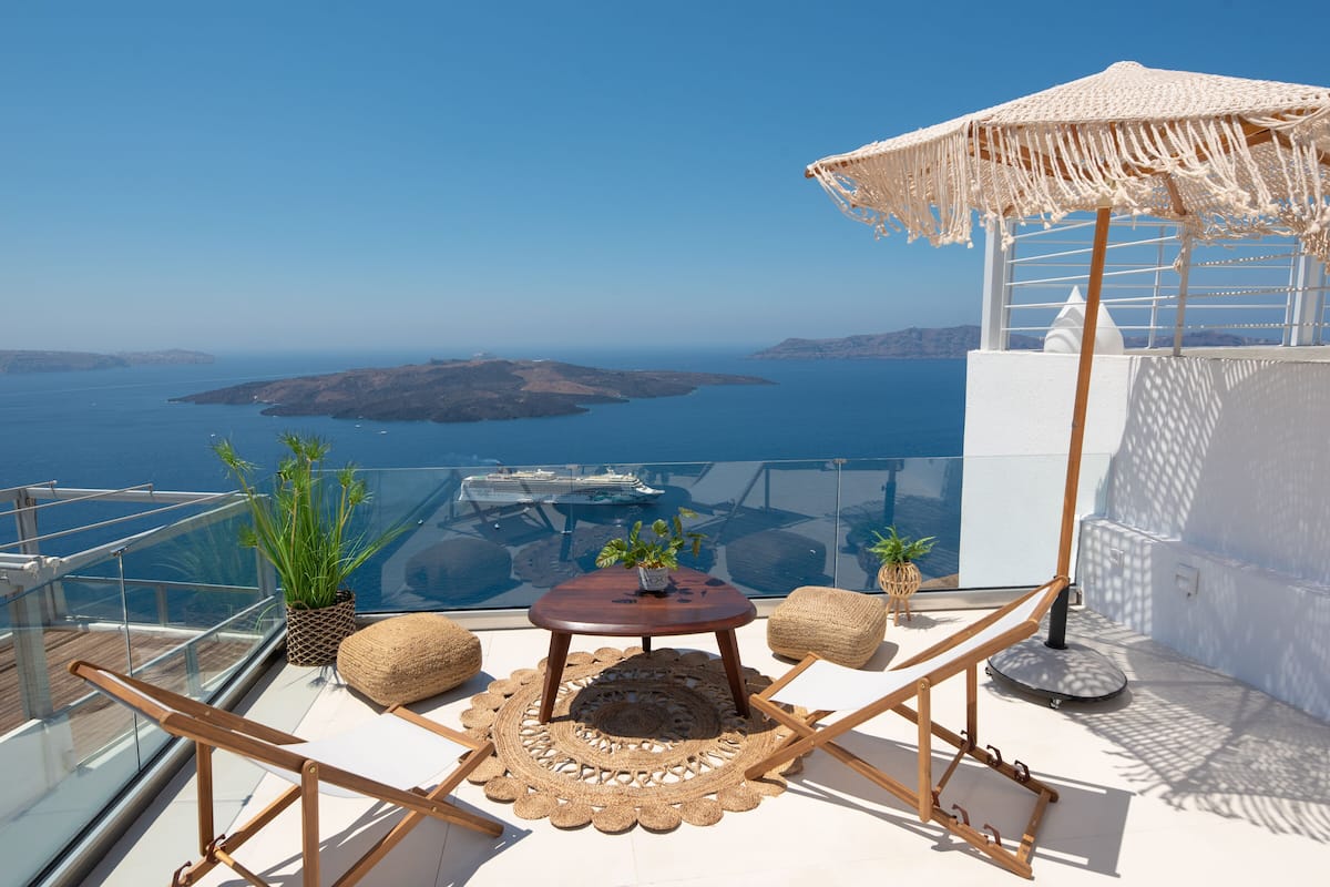 A balcony with a round table, two chairs, a woven rug, and a woven parasol.
