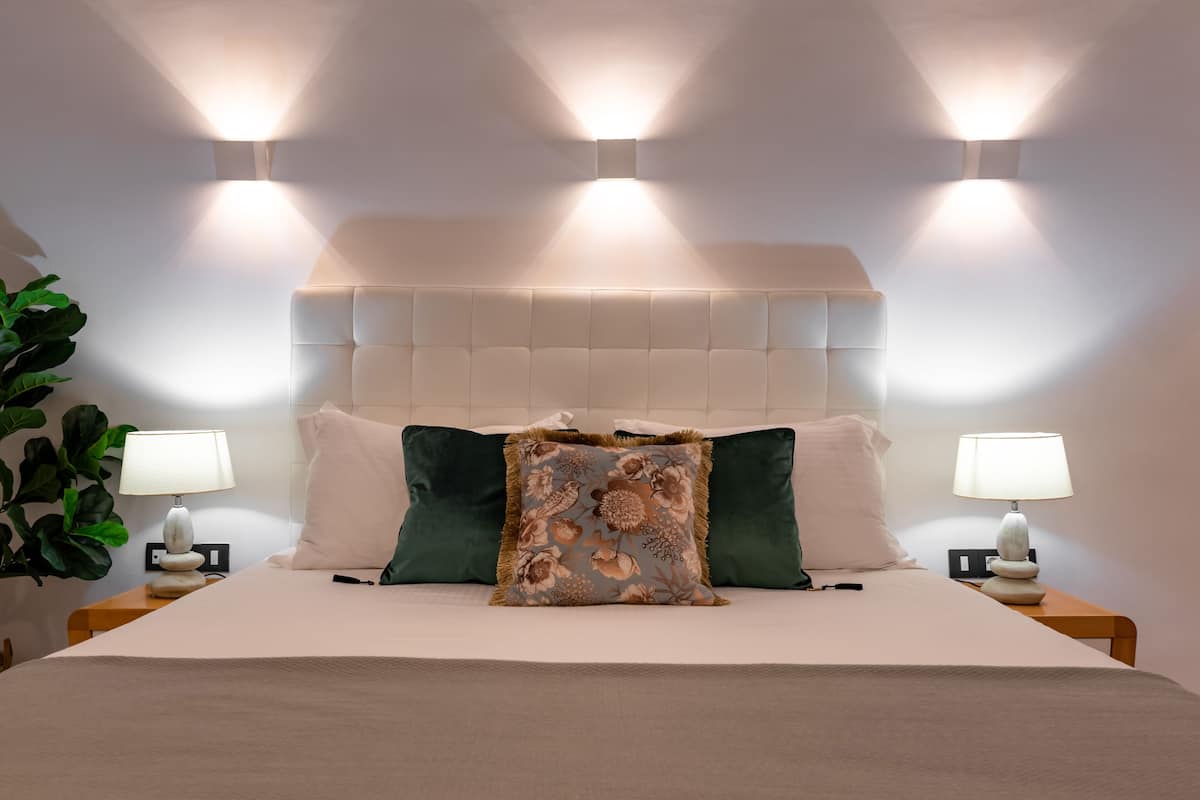 A neatly made bed with a tufted headboard, two bedside lamps, and a floral pillow.