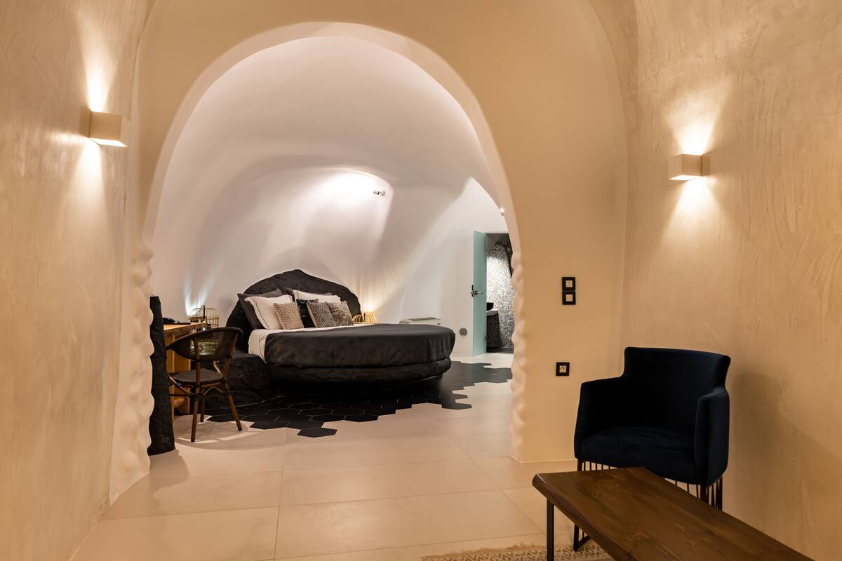 A bedroom with a bed, a chair, a table, and a unique arched ceiling.