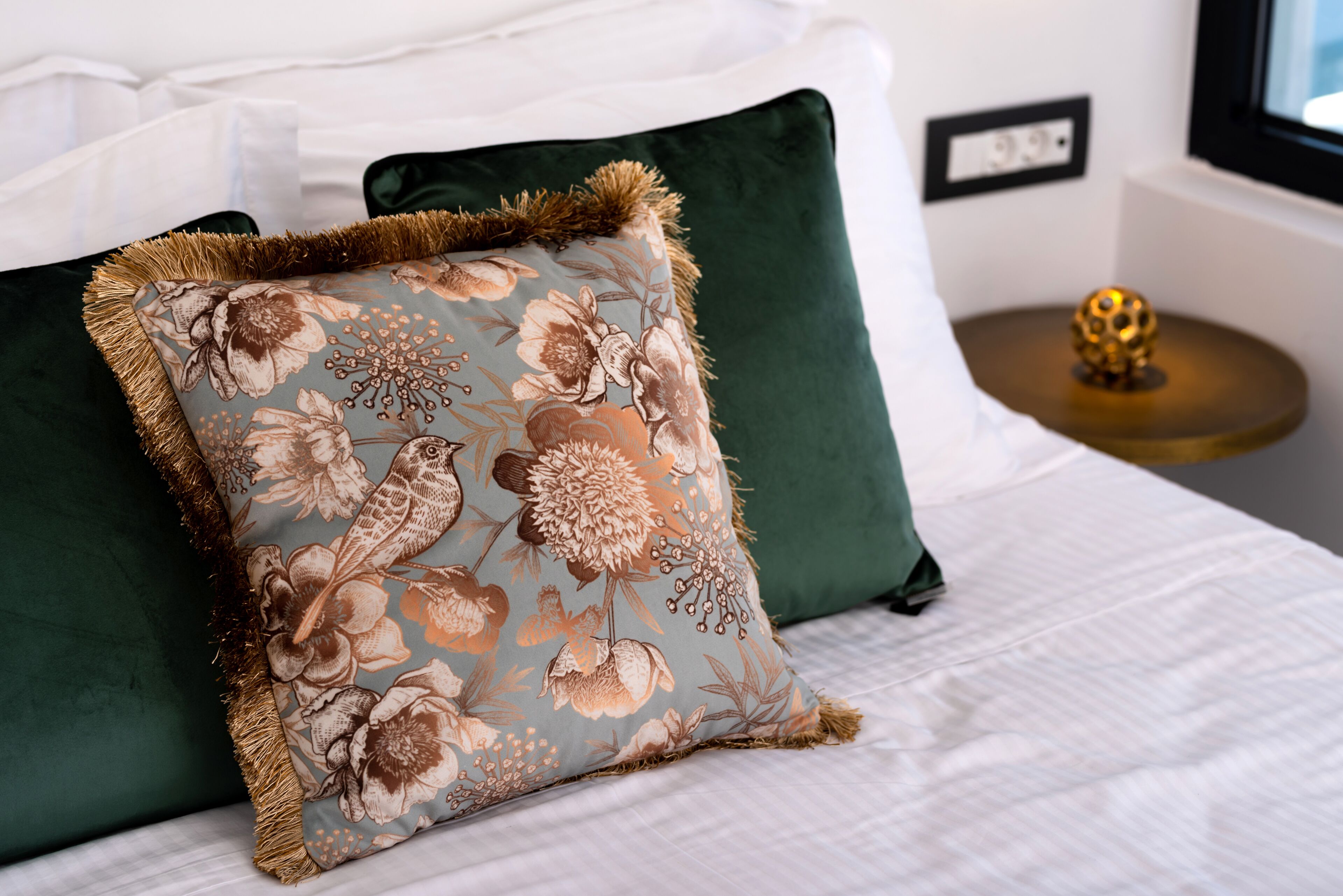 A bed with a floral pillow, a green pillow, and a round table with a golden spherical object.