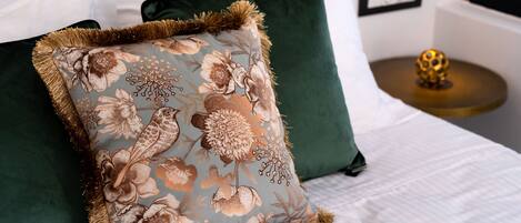 A bed with a floral pillow, a green pillow, and a round table with a golden spherical object.