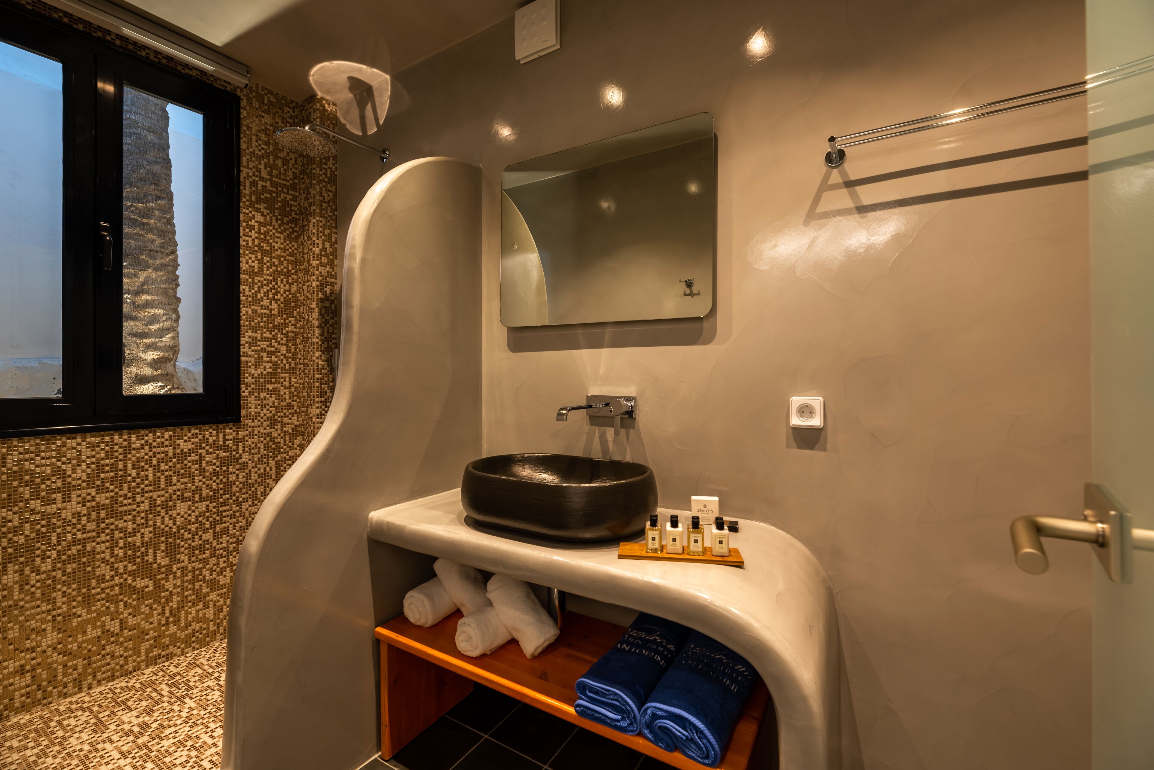 A modern bathroom with a large mirror, a black basin, and neatly folded towels.