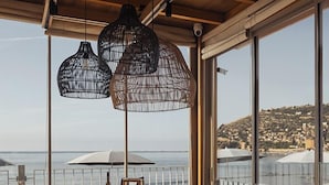 An outdoor dining area with a wooden table and chairs, large windows, and hanging wicker lamps. - En Vie Beach Boutique Hotel - Adult Only (Alanya)