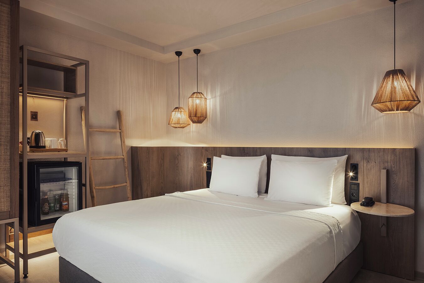 A modern hotel room with a large bed, wooden headboard, bedside tables, and pendant lights.
