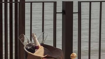 A wooden table with a bottle of champagne, a glass, and decorative vases by a railing overlooking a body of water.
