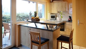 A modern kitchen with a central island, wooden chairs, a microwave, and a view of the outdoors. - Ferienwohnung am Rain (Winden im Elztal)