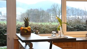 A kitchen counter with a fruit basket, a vase with a plant, and a window with a view of trees and mountains. - Ferienwohnung am Rain (Winden im Elztal)