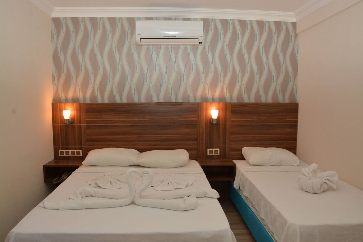 A hotel room with two beds, a wooden headboard, wall-mounted air conditioning, and bedside lamps.