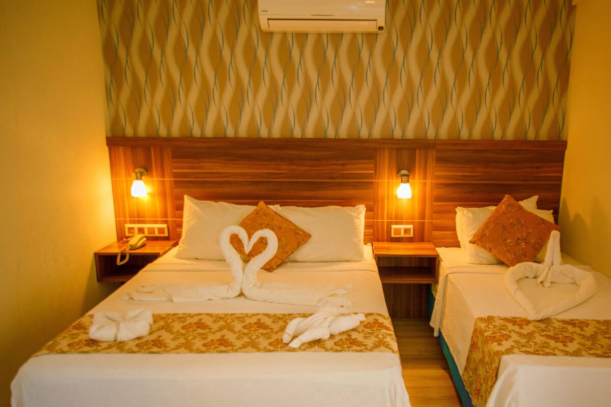 A hotel room with two beds, each with a heart-shaped towel arrangement, wooden headboards, and bedside lamps.