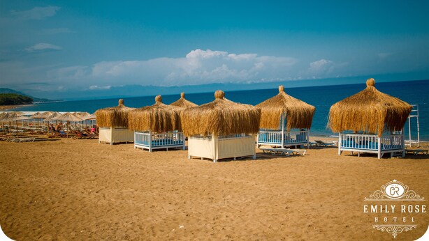 A beach with thatched-roof huts and lounge chairs. - Emily Rose Hotel (Kemer)
