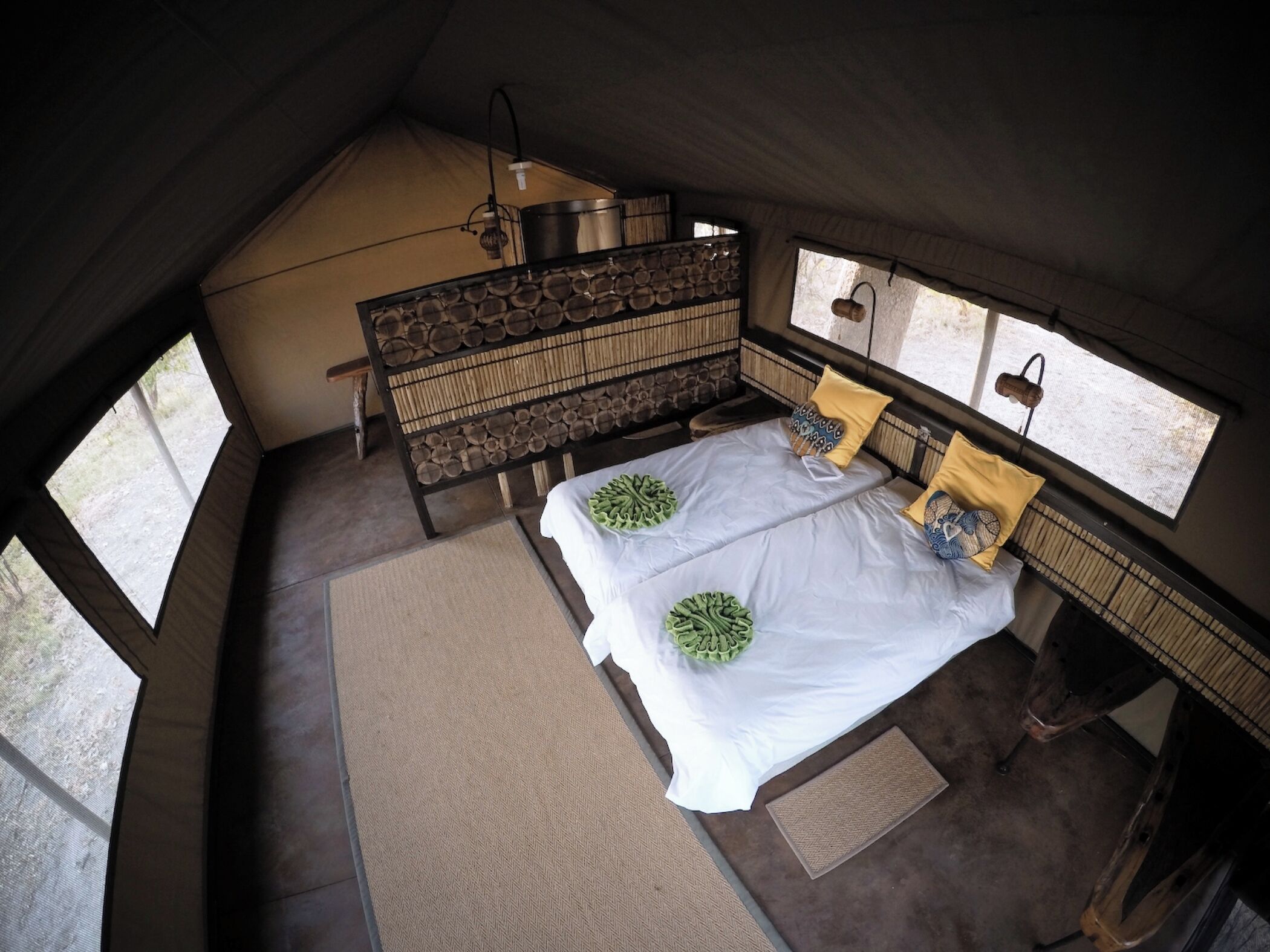 A tented room with two beds, a wooden bench, and a view of the outdoors.