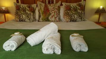 A neatly made bed with floral pillows, a green bedspread, and three rolled towels with gold tags.