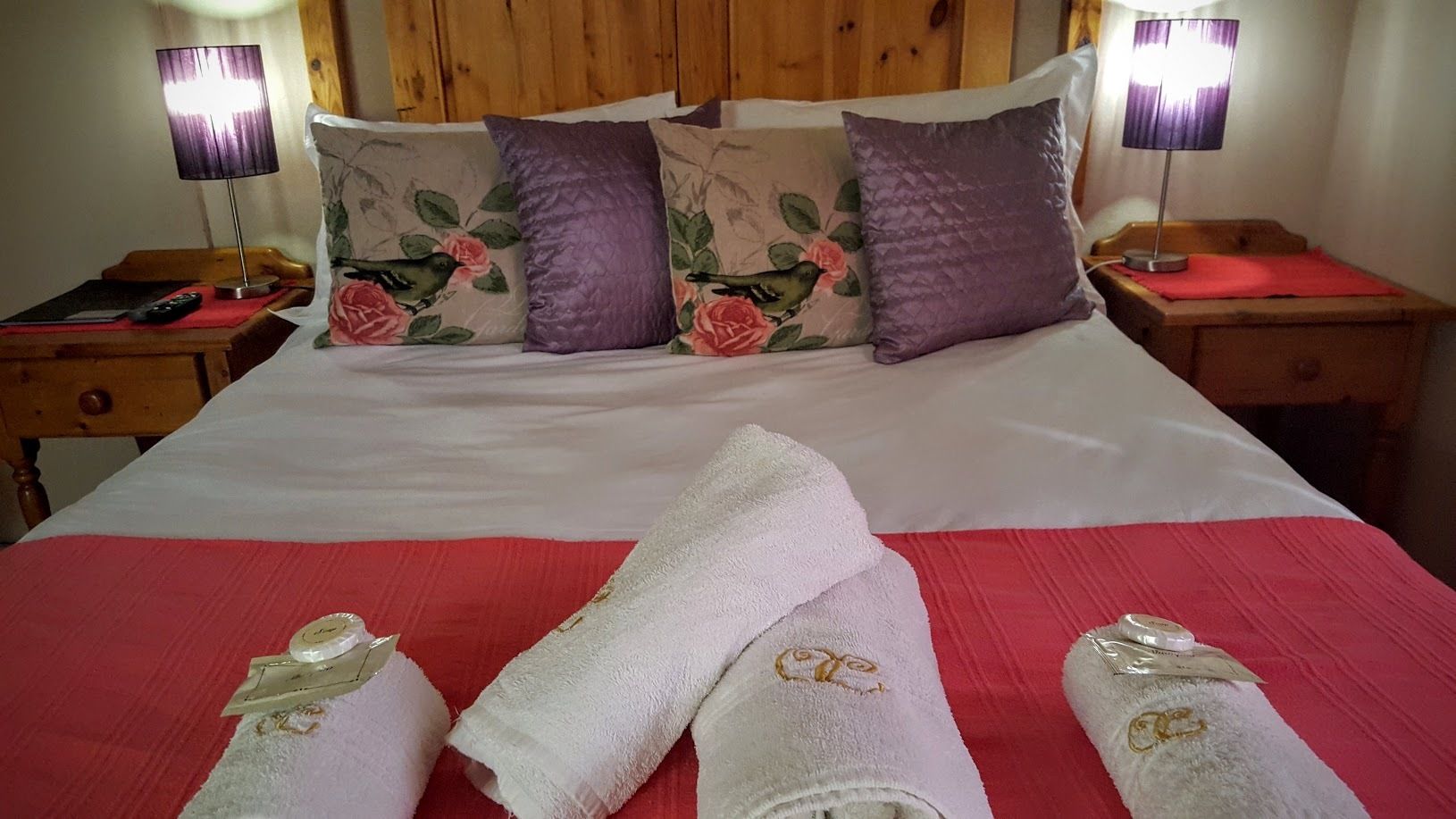 Una cama bien hecha con almohadas estampadas, una colcha roja y dos mesitas de noche con lámparas.