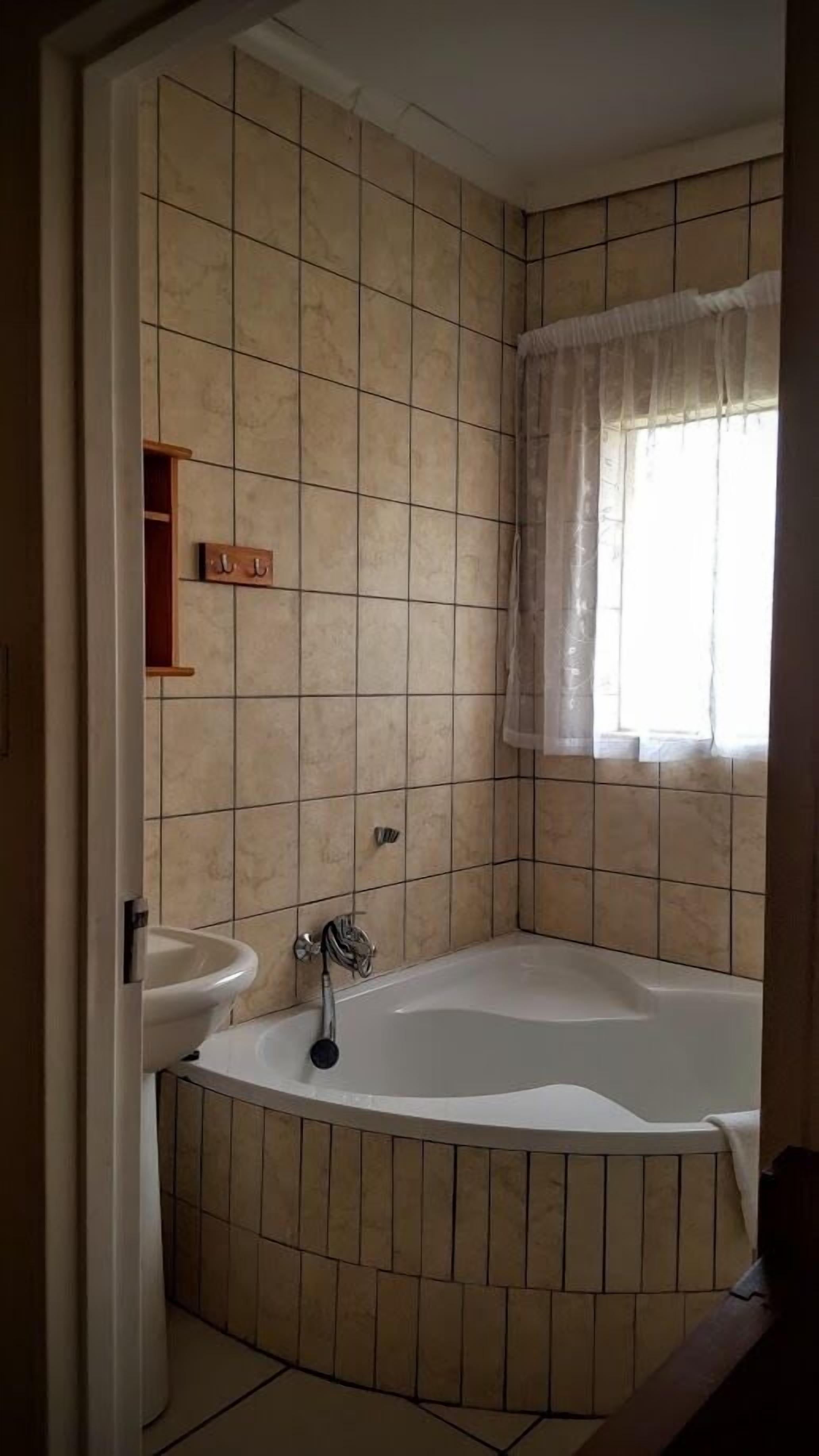 Un baño con bañera, lavamanos y ventana con cortina.