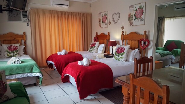 Habitación de hotel con dos camas, cada una con cubrecama rojo y almohadas blancas, cabecero de madera y una silla verde.