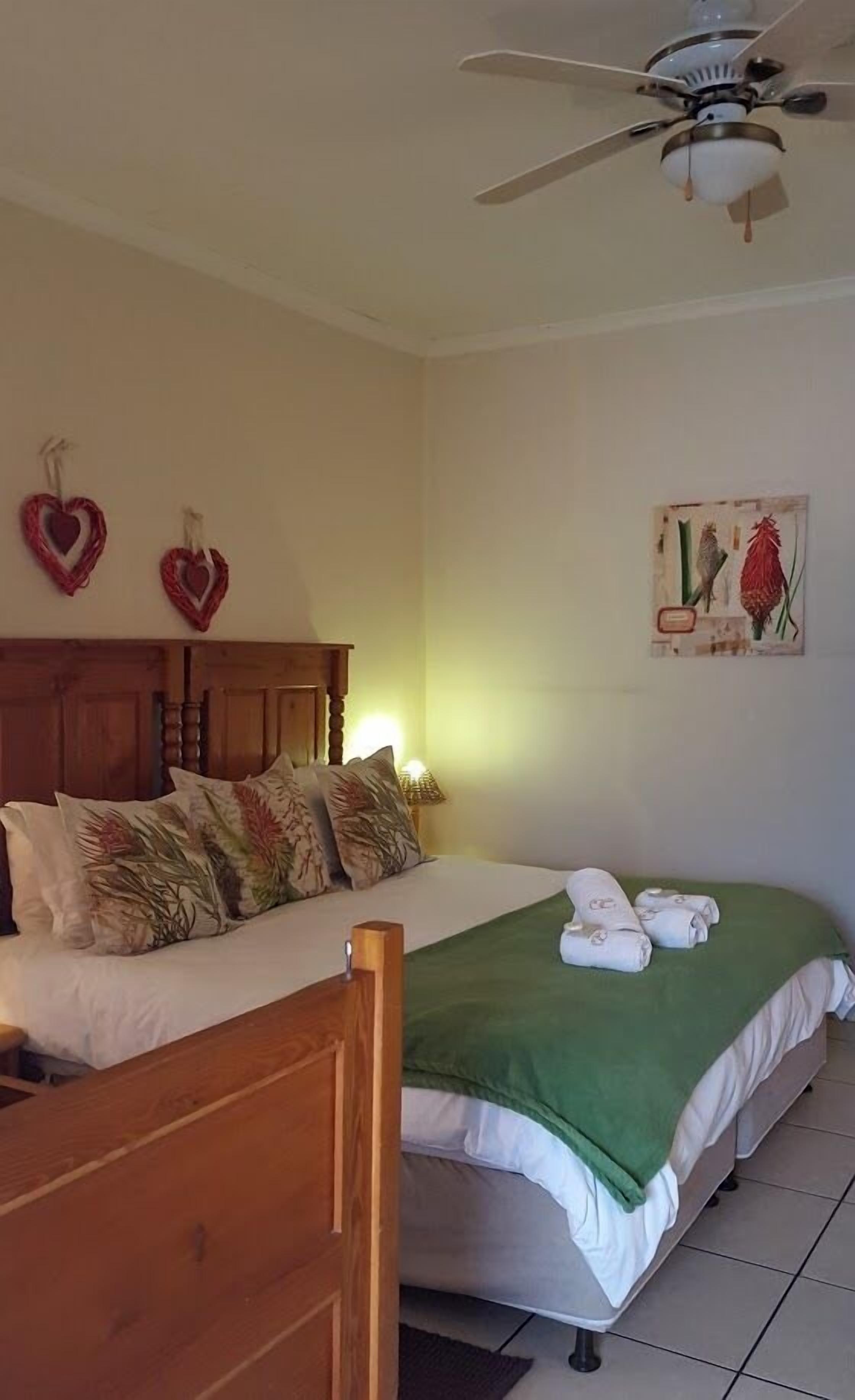 A bedroom with a wooden bed frame, a green blanket, and two heart-shaped decorations on the wall.