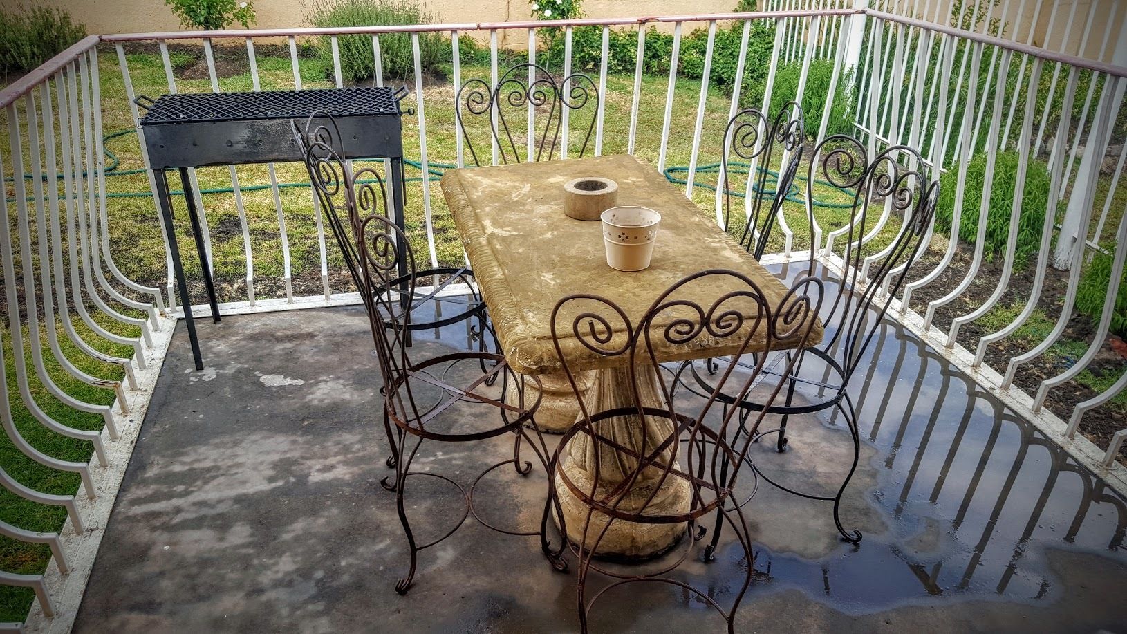 Une terrasse avec une table et des chaises, entourée d’une clôture en métal blanc.
