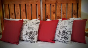 Una cama con cuatro almohadas, dos rojas y dos con estampado floral.
