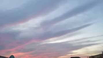 Un ciel au coucher du soleil, avec des nuages au-dessus d’un bâtiment surmonté d’un dôme et orné de drapeaux.