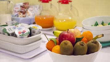 A table with a bowl of fruits, a glass of orange juice, and a container of yogurt.