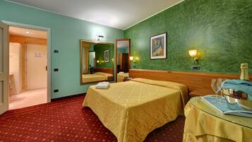 Habitación de hotel con dos camas, un espejo, un cuadro y una mesa con una botella y vasos.